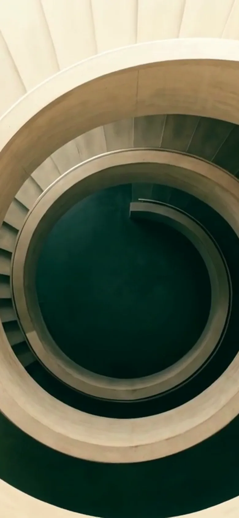 O scară spirală de beton văzută de sus, cu treptele convergând spre un centru verde-închis.